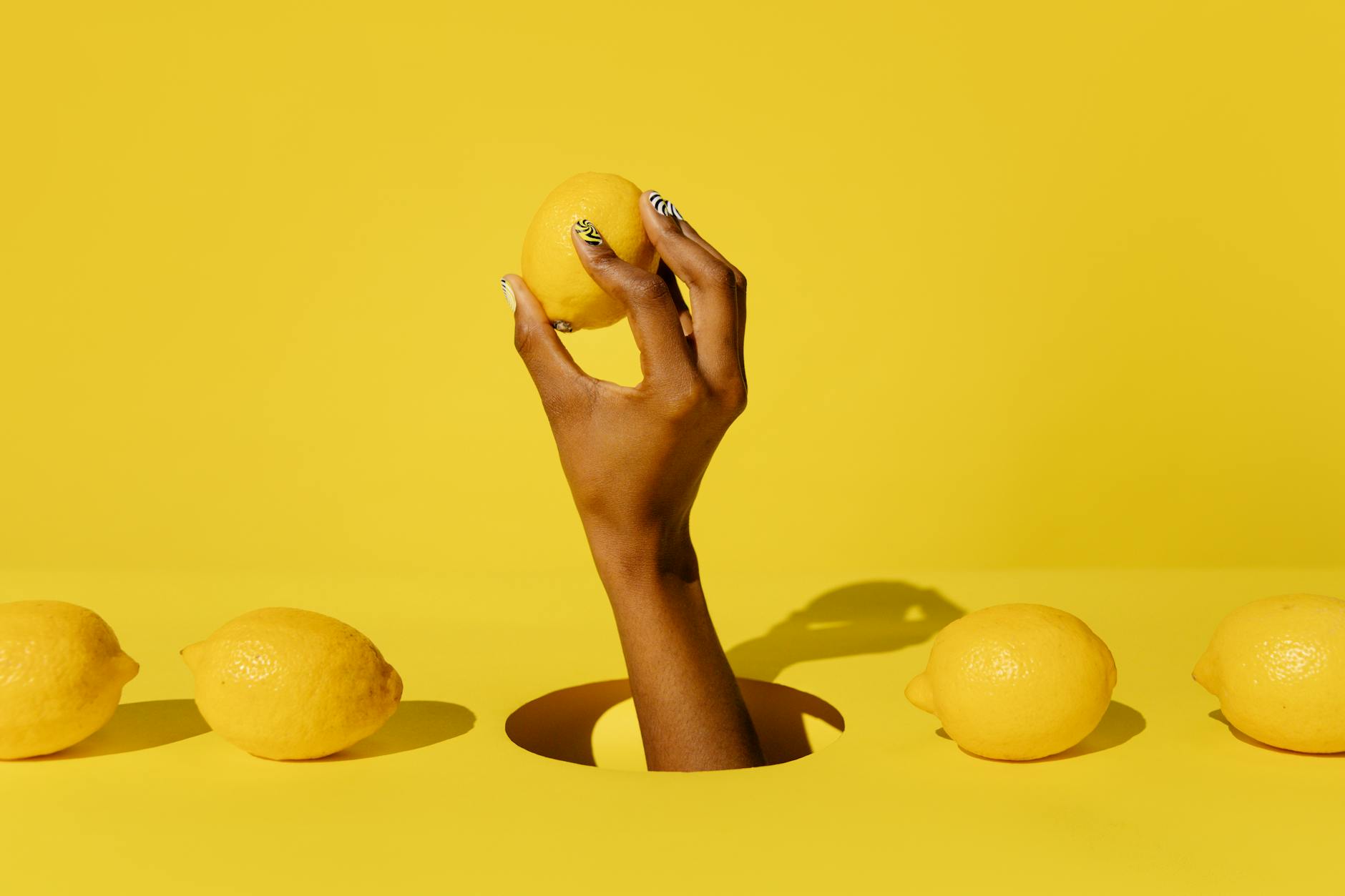 Hand holding a fresh lemon against a bright yellow background, symbolizing simplicity and natural pleasure