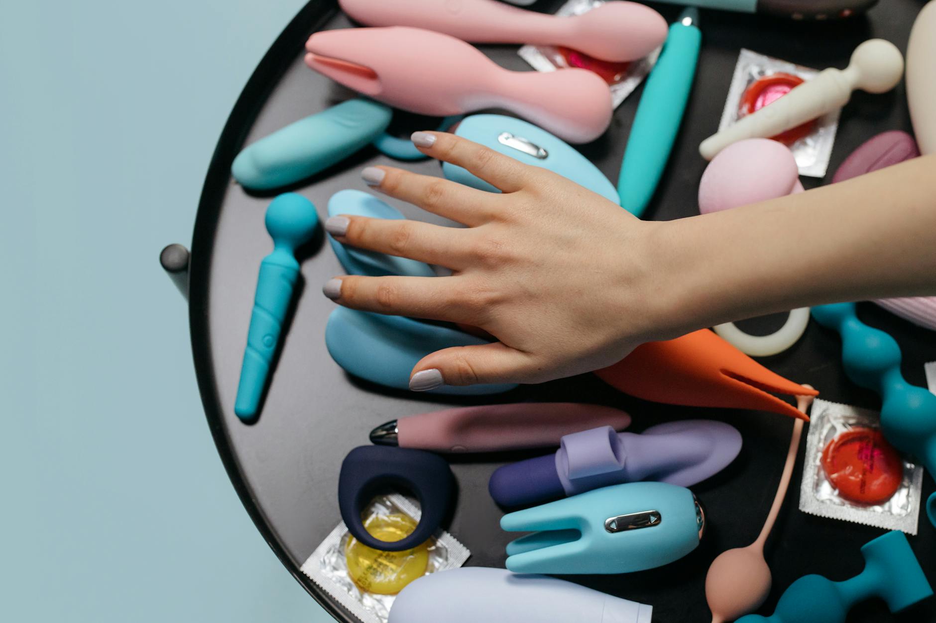 Una mano raggiunge una varietà di vibratori colorati disposti su un tavolo.
