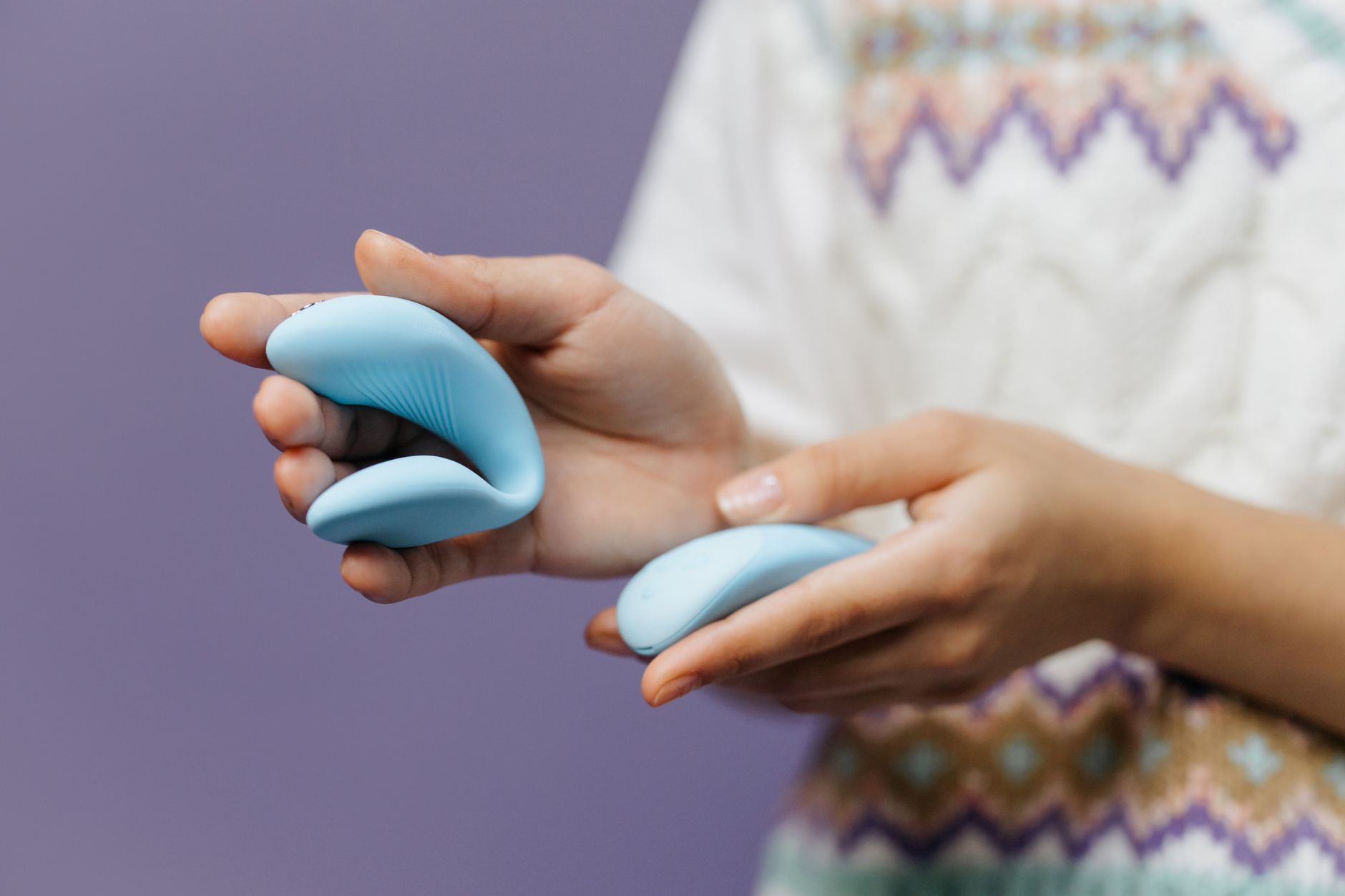A close-up of hands holding a sleek blue vibrator against a purple background.