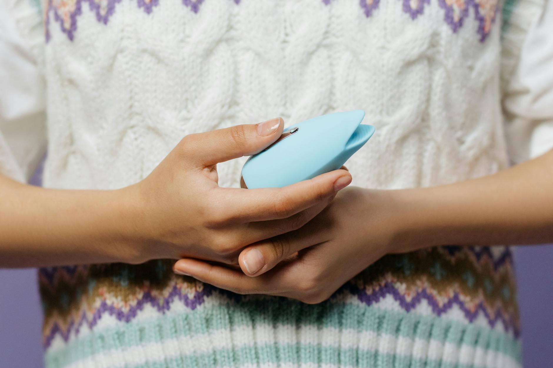 Close-up of hands holding a blue personal vibrator against a knitted sweater.